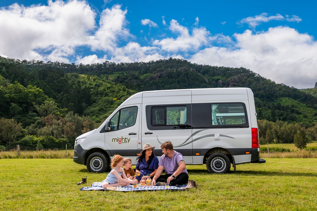 Family having a picnic beside a campervan in the green hills of Queensland, Australia