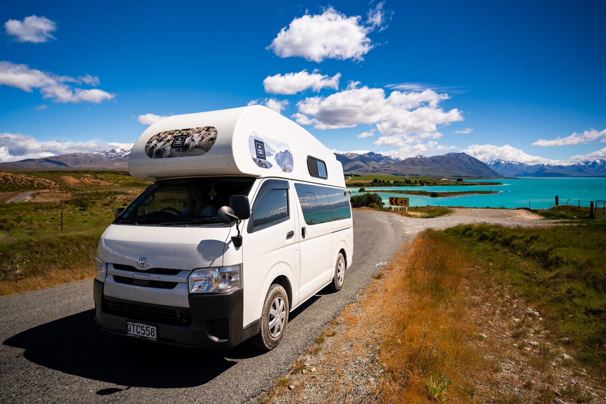 Waka Campa hi-top campervan on a gravel road by a turquoise lake in New Zealand