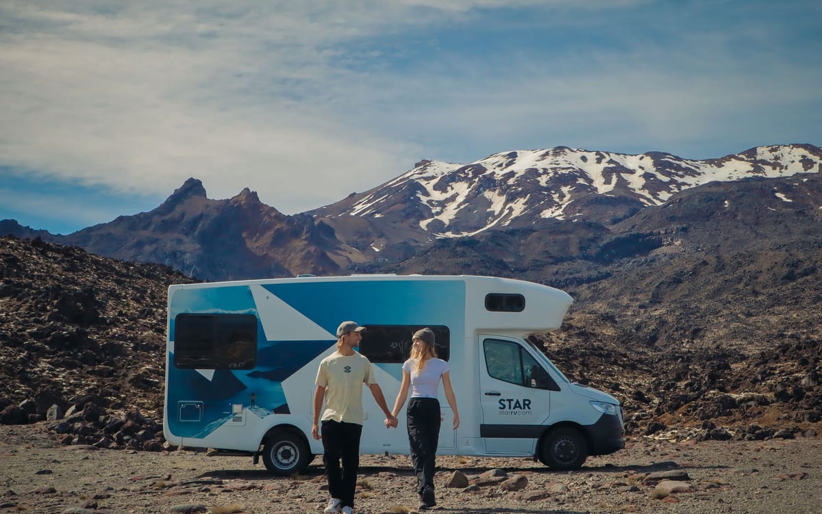 Couple walking beside a Star RV motorhome with snowy volcanic peaks in New Zealand